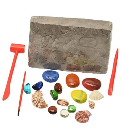 Bloco de areia com pegadas e ferramentas de escavação, várias pedras coloridas e conchas ao redor, usado para atividades de arqueologia educativa.