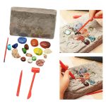Conjunto de pedras preciosas de diferentes cores e tamanhos, ferramentas de escavação, e uma placa de areia para escavação.