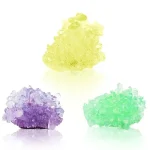 Três cristais coloridos em tons de amarelo, roxo e verde, com textura cristalina, sobre fundo branco.