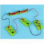 Componentes de um kit de eletricidade infantil com fios, pilhas, lâmpadas e interruptores em bases verdes.