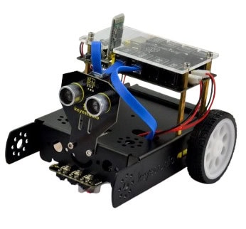 Robô com sensores de proximidade, rodas brancas, estrutura preta, componentes eletrónicos visíveis, e cabos coloridos, usado para ensino de robótica infantil.