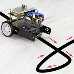 Robô com rodas, sensores de linha, cabos azuis e componentes eletrónicos, a seguir uma linha preta no chão branco.
