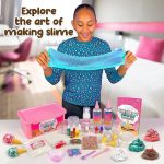 Menina sorridente segurando slime azul transparente, com vários ingredientes e acessórios de slime na mesa.
