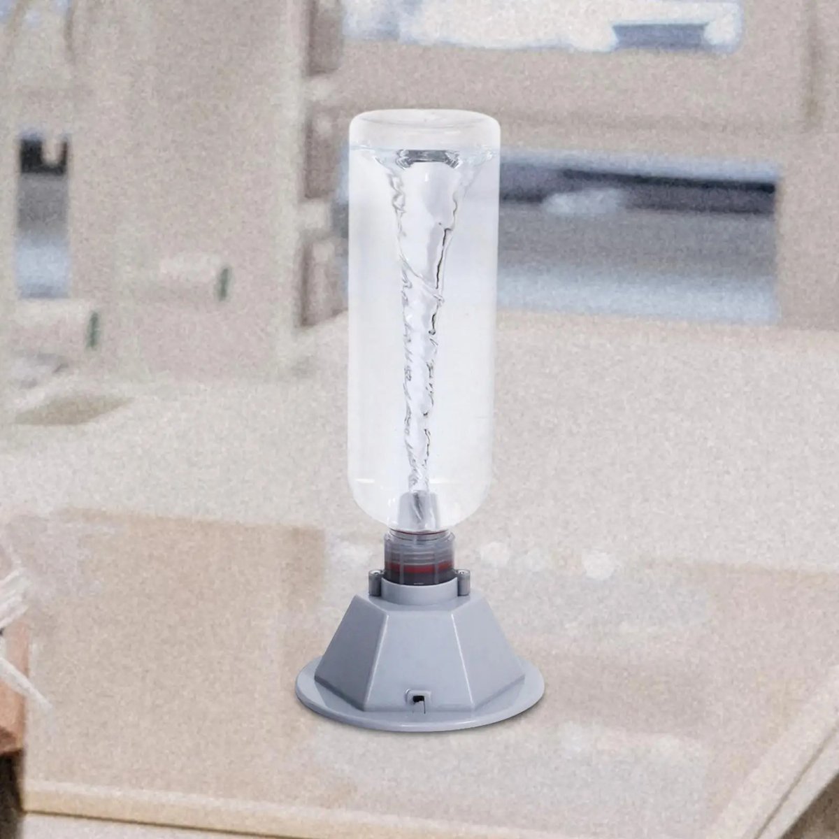 Experiência Tornado em funcionamento Tubo de vidro com tornado visível dentro, apoiado numa base cinzenta, em ambiente de laboratório ou sala de aula.