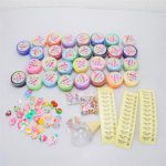 Vários potes de slime com cores diferentes, pequenos enfeites, pérolas coloridas, e instruções para fazer slime, dispostos sobre uma mesa branca.