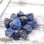 Vários pedaços de lápis-lazúli bruto com tons de azul e detalhes minerais, exibidos sobre uma superfície de madeira clara.