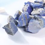 Vários pedaços de lápis-lazúli em bruto com tons de azul e detalhes dourados, exibidos sobre uma superfície branca.