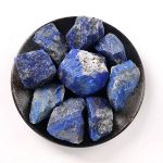 Vários pedaços de lápis-lazúli em bruto com tons de azul intenso e detalhes minerais, apresentados numa tigela preta.