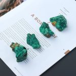 Quatro pedaços de malaquite bruta de diferentes tamanhos e formas, colocados sobre uma revista com texto em português.