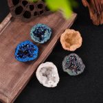Conjunto de cinco mini geodos de cristal de rocha em várias cores e texturas, exibidos sobre uma tábua de madeira com elementos decorativos ao fundo.