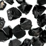Amostras de obsidiana em bruto com superfícies brilhantes e formas irregulares, exibindo a textura vítrea e a cor preta brilhante típica do mineral.