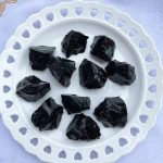 Pedras de obsidiana bruta de forma irregular, de cor preta brilhante, dispostas numa travessa branca com detalhes de corações.