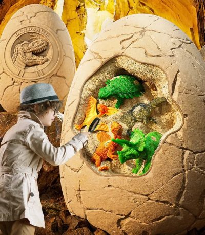 Criança a escavar brinquedos de dinossauros coloridos dentro de um ovo de grande dimensão, com ambiente de escavação de fósseis.