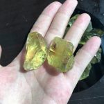 Duas pedras de citrino em bruto, de cor amarela translúcida, com superfícies irregulares e texturas naturais, seguradas na palma de uma mão.