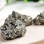 Três amostras de pirite em bruto com superfície brilhante e textura granular, exibindo o seu brilho metálico prateado.