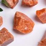 Vários fragmentos de pedra do sol em bruto, com tonalidades alaranjadas e textura áspera, exibidos sobre fundo branco.