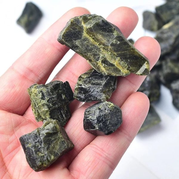 Vários fragmentos de turmalina verde com superfícies brilhantes e texturadas, alguns com tonalidades mais escuras e outros mais claras, em fundo branco.