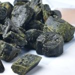 Vários fragmentos de turmalina verde com superfícies irregulares e detalhes minerais visíveis, alguns com tonalidades mais escuras e outros com manchas mais claras.