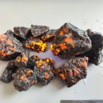 Conjunto de pedras Yooperlite com fluorescência laranja e amarela sob luz UV, destacando-se na superfície branca.