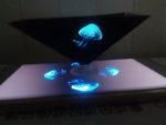 Holograma de uma medusa azul projetada em um dispositivo com luzes brilhantes e efeito de água, visto de cima.