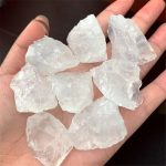 Vários cristais de quartzo branco em bruto, com superfícies irregulares e translúcidas, segurados na palma da mão.