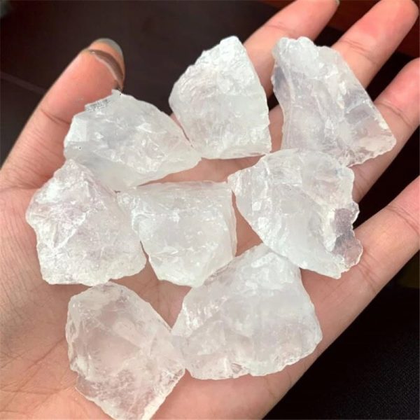 Vários cristais de quartzo branco em bruto, com superfícies irregulares e translúcidas, segurados na palma da mão.