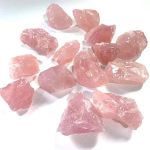 Vários cristais de quartzo rosa brutos, com superfícies irregulares e cor rosa suave, dispostos sobre fundo branco.