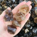 Vários pedaços de quartzo fumado em bruto, com cores que variam do castanho claro ao escuro, mostrando diferentes formas e tamanhos, com superfícies polidas e naturais.