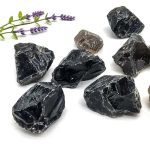 Vários pedaços de quartzo fumado em bruto, com diferentes tamanhos e formas, sobre fundo branco, acompanhado de raminho de lavanda.