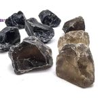 Vários cristais de quartzo fumado em bruto, com cores que variam do preto ao cinza claro, exibindo texturas naturais e formas irregulares.
