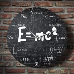 Relógio de parede com fundo preto, coberto de fórmulas matemáticas e físicas em branco, com ponteiros brancos e destaque para a equação E=mc² no centro.