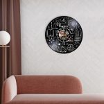Relógio de parede preto com desenhos de conceitos de física, incluindo átomos, fórmulas e instrumentos científicos, decorando uma parede de sala moderna.