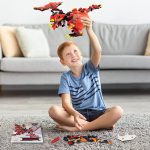 Menino com cabelo ruivo brincando com robô de construção vermelho e preto feito de peças de LEGO, sentado no chão de uma sala moderna.