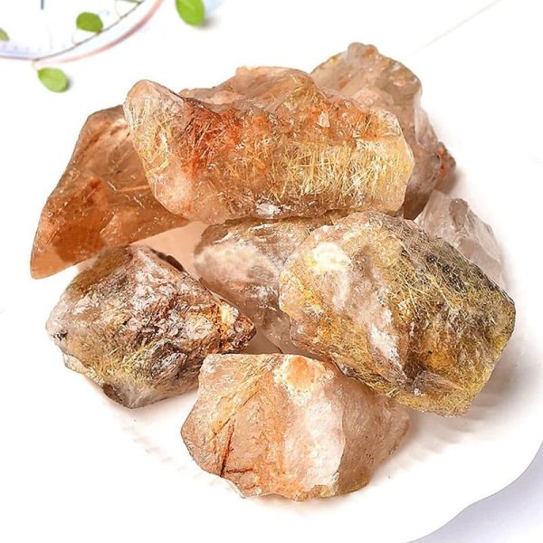 Vários cristais de rutilo em bruto com agulhas douradas visíveis, cores que variam entre laranja, amarelo e transparente, com textura irregular e superfície brilhante.