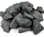 Pedras de shungite bruta de várias formas e tamanhos, com textura escura e superfície irregular, usadas em decoração e estudos científicos.