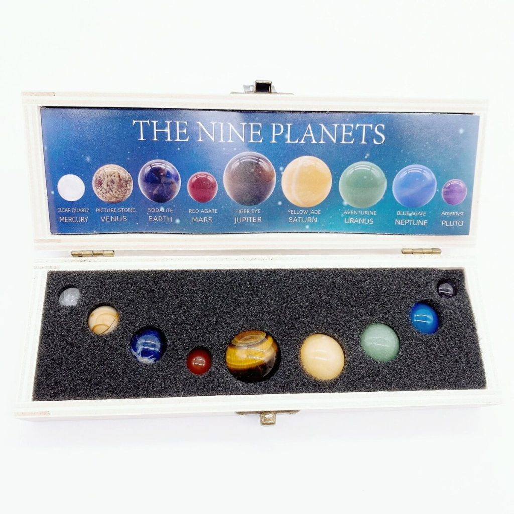 Conjunto de nove pedras preciosas representando os planetas do sistema solar, cada uma com cores distintas, em uma caixa com descrição dos planetas.
