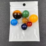 Conjunto de pequenas pedras preciosas coloridas representando planetas do sistema solar, incluindo Terra, Marte, Júpiter, Saturno, Urano, Netuno, Mercúrio e Vénus, em saco plástico transparente.