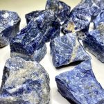 Vários pedaços de sodalita em bruto com tons azuis e detalhes brancos, mostrando texturas naturais e formas irregulares.