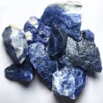 Conjunto de pedras de sodalita em bruto, com cores azul escuro, branco e preto, mostrando diferentes formas e tamanhos, com textura natural e superfícies irregulares.