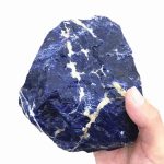 Pedra de sodalita bruta com superfície irregular, cor azul intenso com veios brancos e detalhes minerais visíveis.