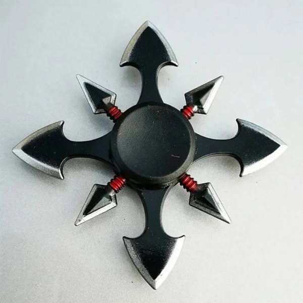 Fidget spinner com design de kunai, pontas afiadas e detalhes vermelhos, visto de cima, em fundo cinzento claro.