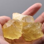 Quatro cristais de topázio amarelo em bruto, com superfícies irregulares e translucidez, sendo segurados por uma mão.