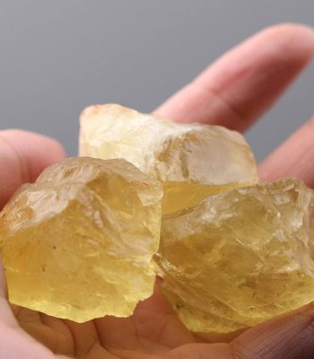 Quatro cristais de topázio amarelo em bruto, com superfícies irregulares e translucidez, sendo segurados por uma mão.