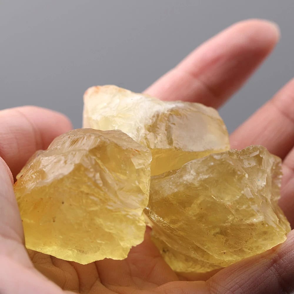 Quatro cristais de topázio amarelo em bruto, com superfícies irregulares e translucidez, sendo segurados por uma mão.