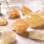 Vários cristais de topázio amarelo em bruto, com formas irregulares e superfícies translúcidas, sobre uma superfície clara.