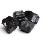 Quatro cristais de turmalina negra em bruto, com superfícies estriadas e textura sólida, sobre fundo branco.