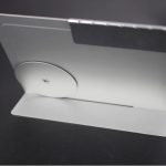 Base de suporte metálica com roda de ajuste para calendário perpétuo em metal, vista lateral, com fundo escuro.