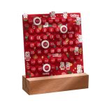 Calendário perpétuo infantil com botões redondos para dias, meses e dias da semana, decorado com coelhinhos e flores, em fundo vermelho, apoiado numa base de madeira.