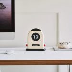 Relógio de calendário perpétuo de mesa com display digital, mostrando o dia 10 de novembro, em ambiente de escritório minimalista.