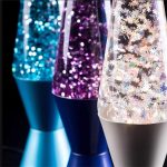 Três lâmpadas de lava com brilhos coloridos e efeitos de neve, em diferentes cores e ângulos, destacando os detalhes das partículas brilhantes e a transparência do líquido.